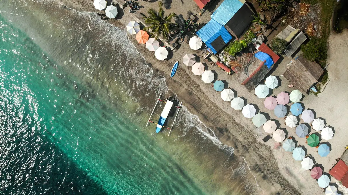 Aerial view of a vibrant Bali beach with colorful umbrellas and turquoise waters.